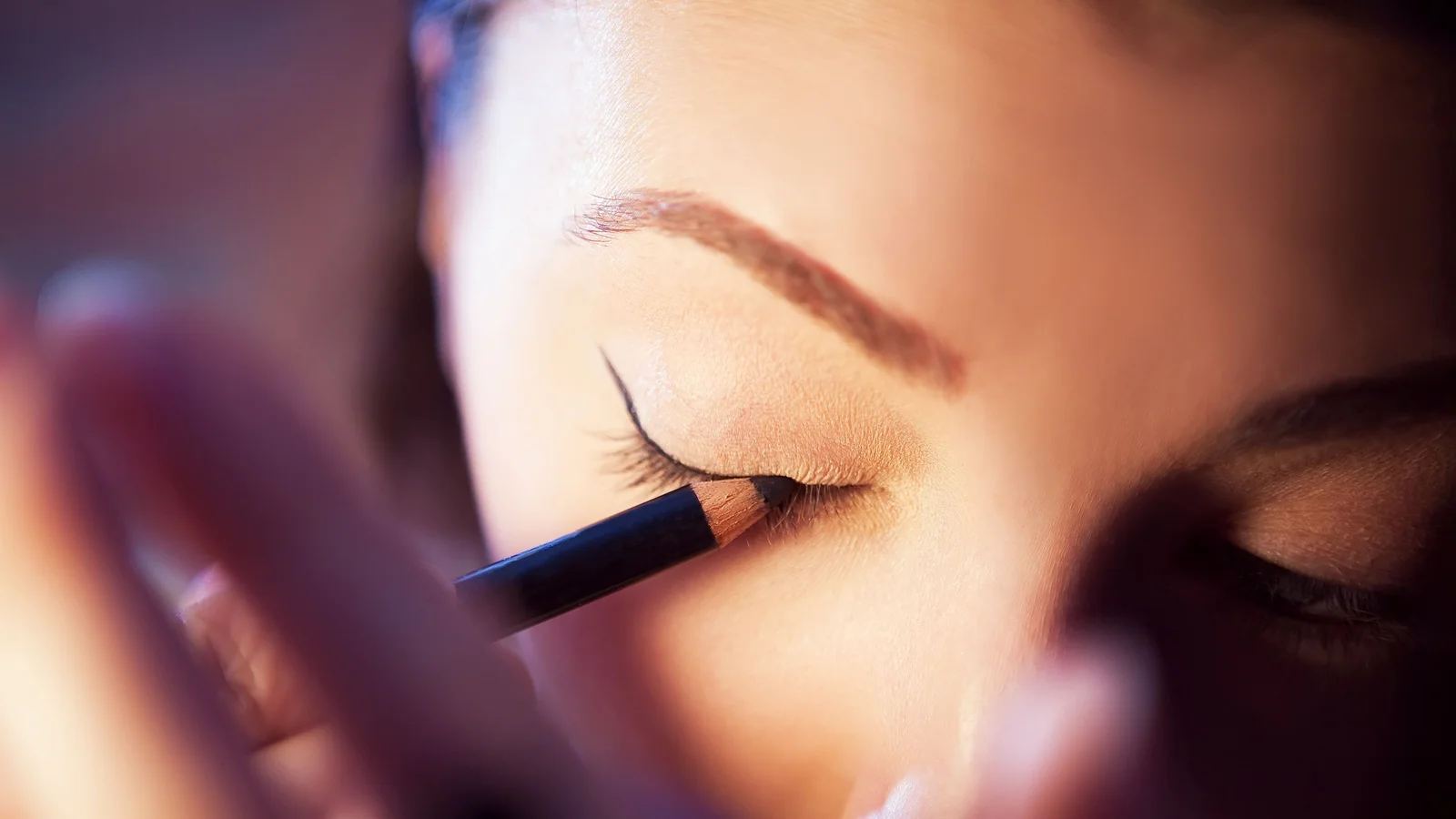 Close-up of a woman drawing eyeliner along her upper eyelid.