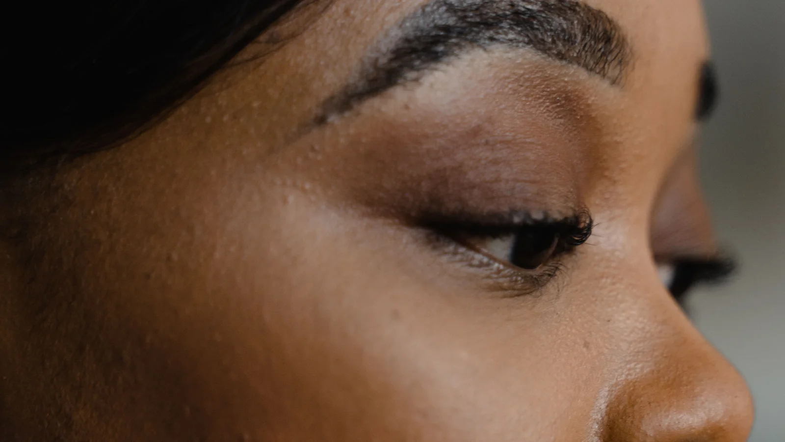 Side profile of a woman with softly defined make-up and visible natural skin texture.