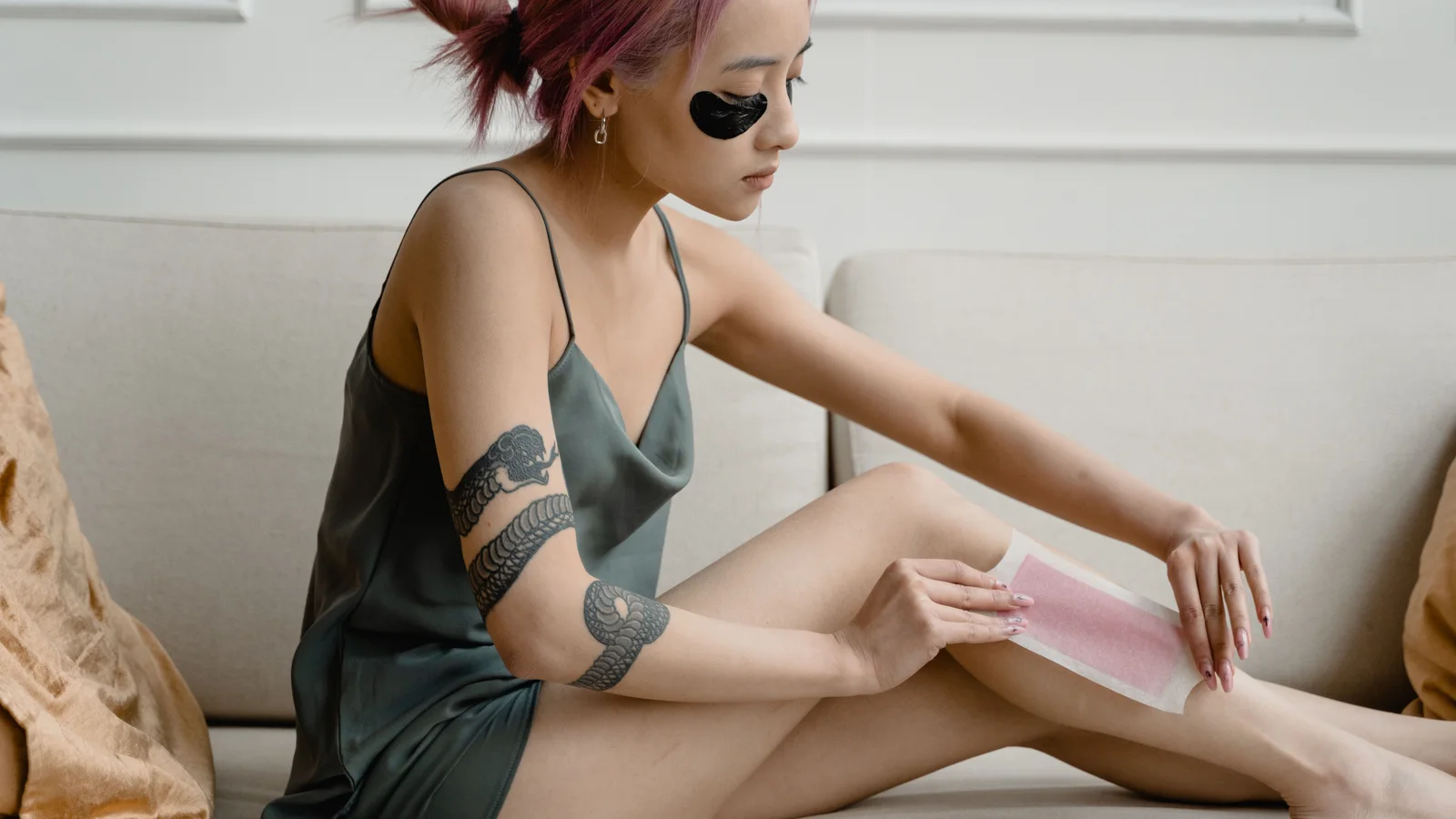 A tattooed woman pressing a wax strip onto her lower leg.