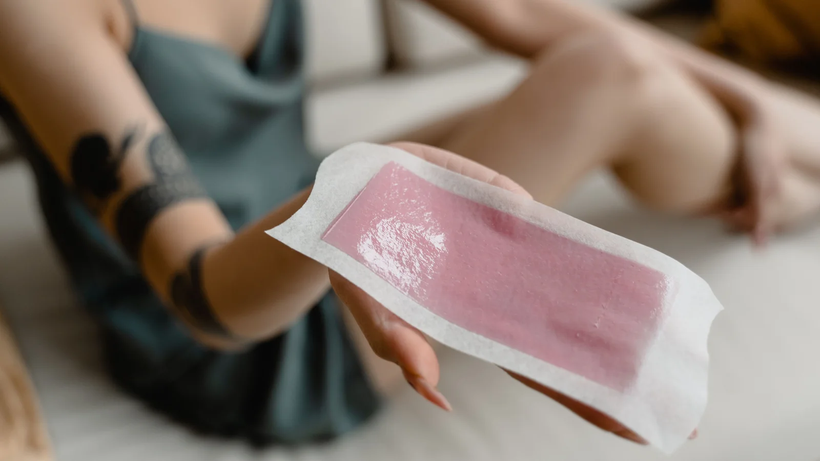A hand holding a used pink wax strip in the foreground.