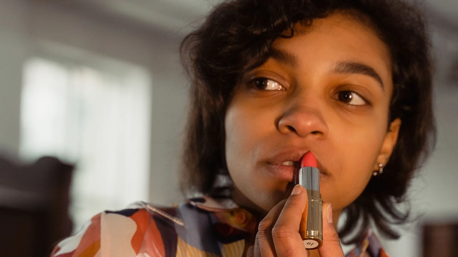 A woman applying lipstick while looking towards a mirror.