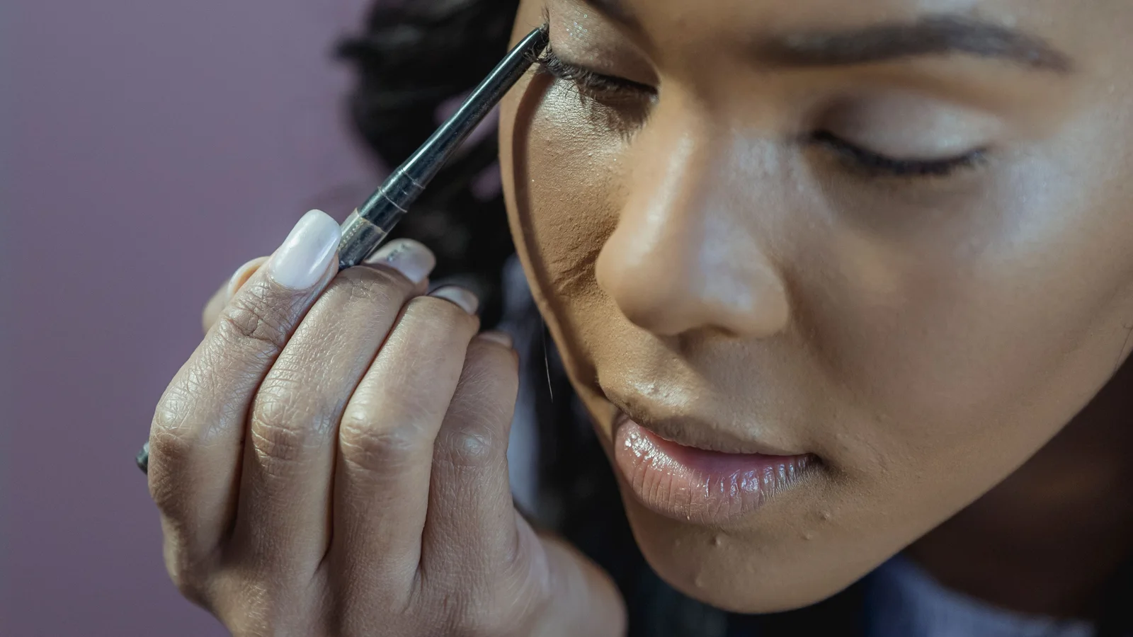 A woman applying make-up beneath one eye with a small brush.