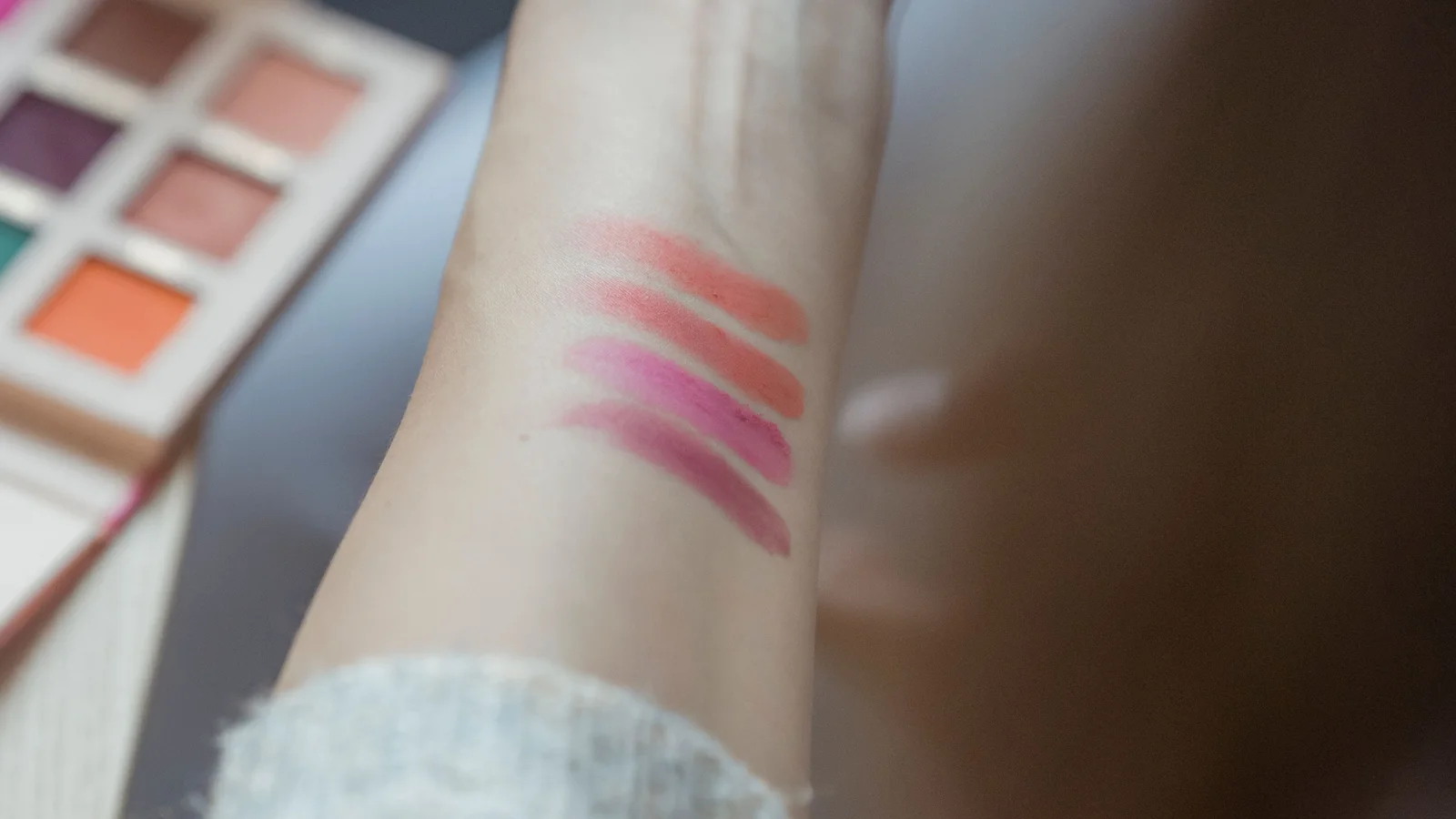 Several cosmetic colour strokes on a forearm beside an open palette.