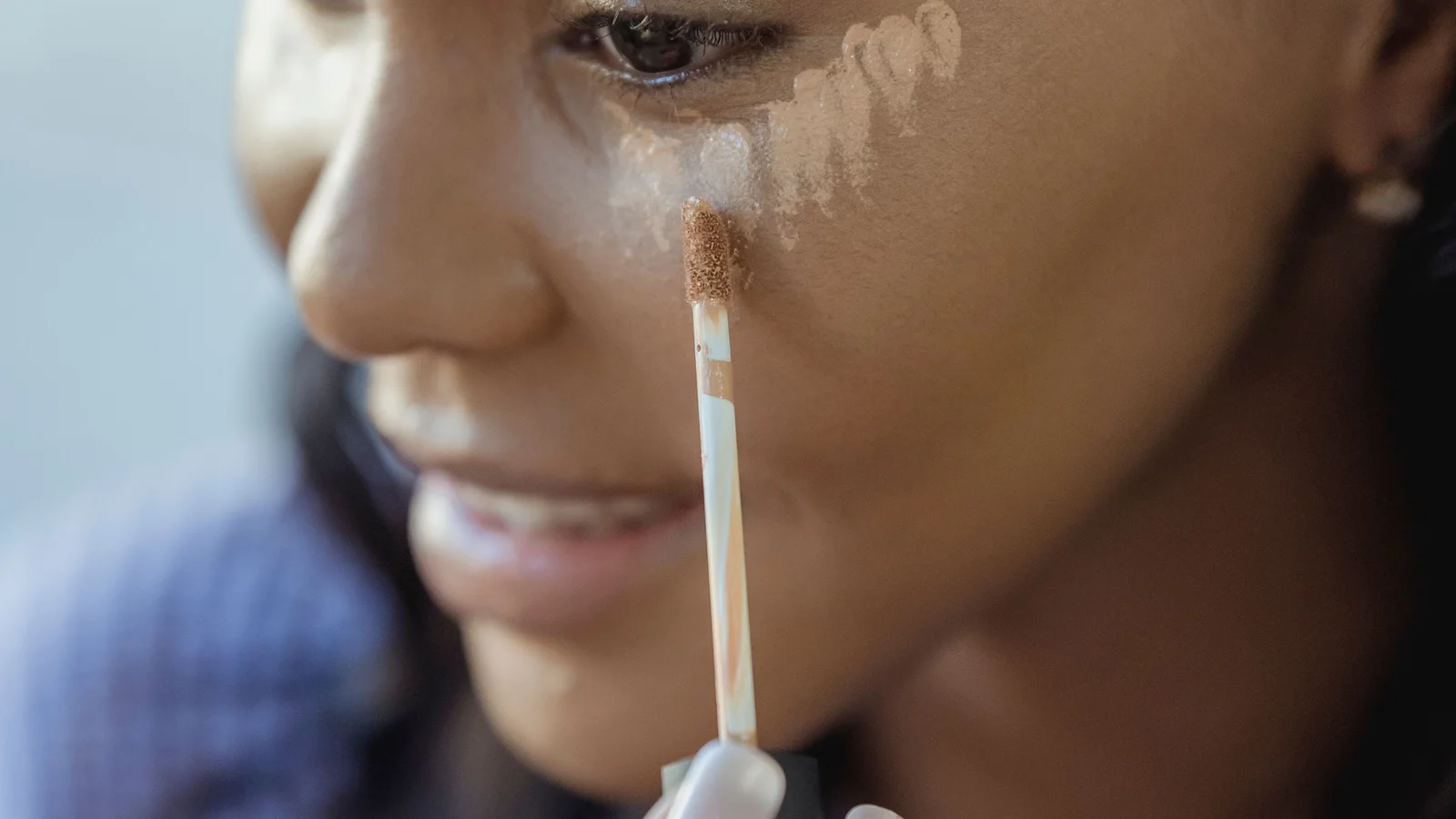 A woman placing concealer beneath her eye with a wand applicator.