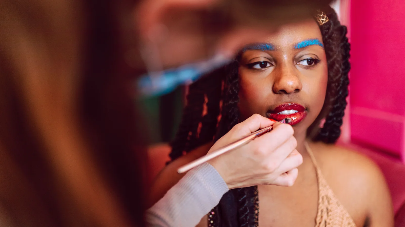 A make-up artist applying red lip colour to a woman with bright blue brows.