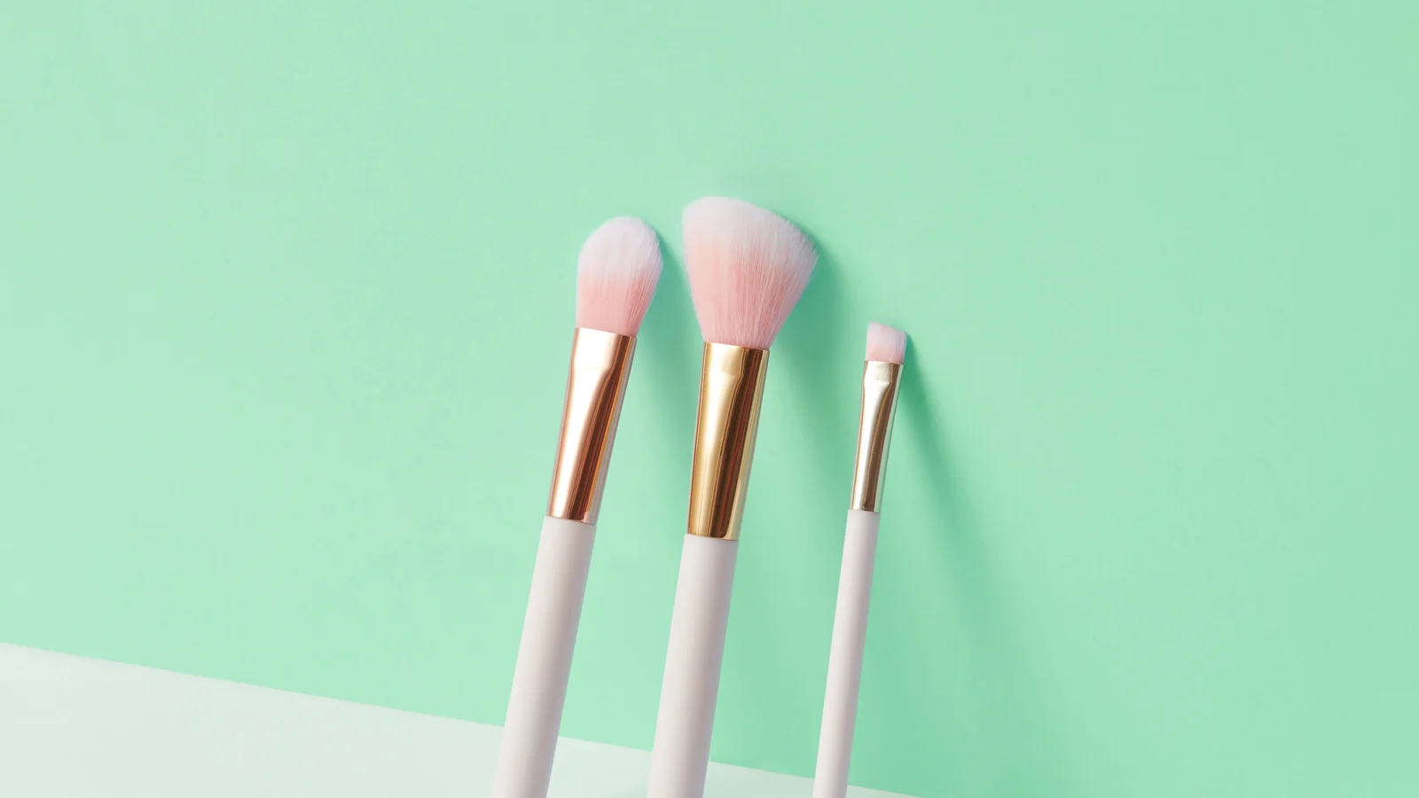 Three make-up brushes arranged on a pale green background.