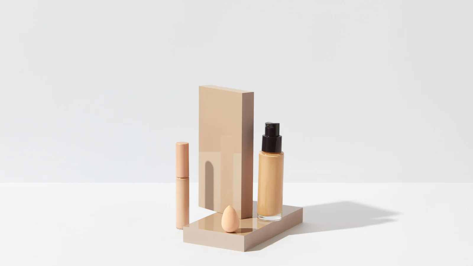 A pump bottle, tube and rectangular cosmetic case on a pale stand.