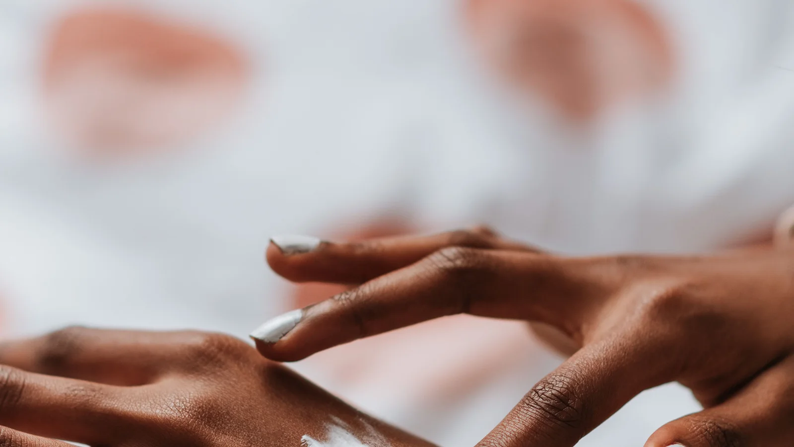 A hand spreading a small amount of cream across the back of another hand.
