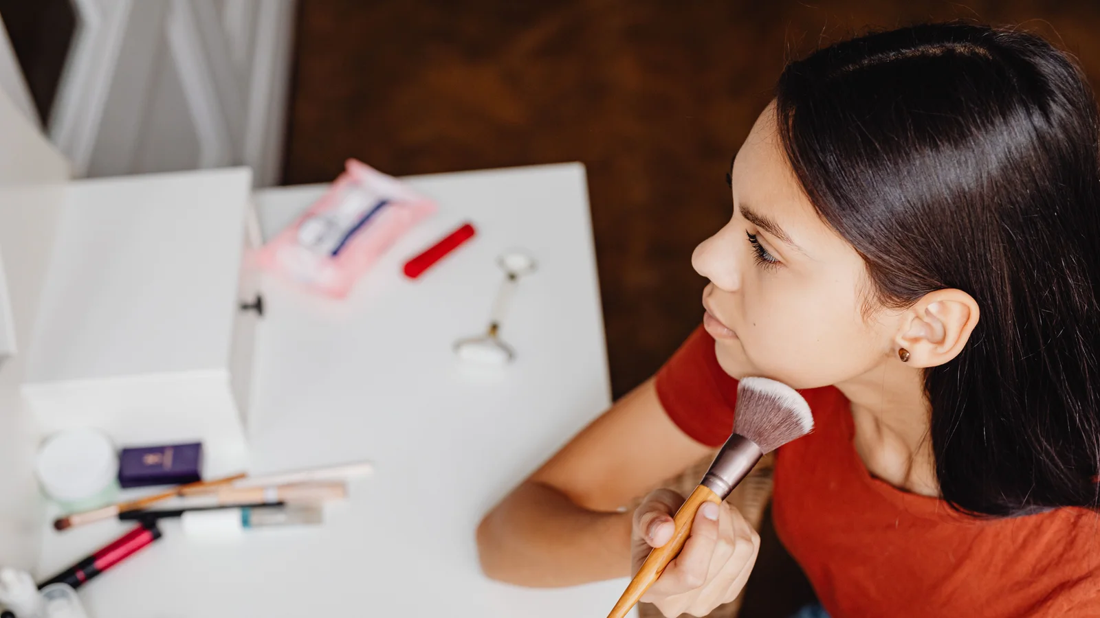 A woman brushing make-up along her jaw while looking towards a mirror.