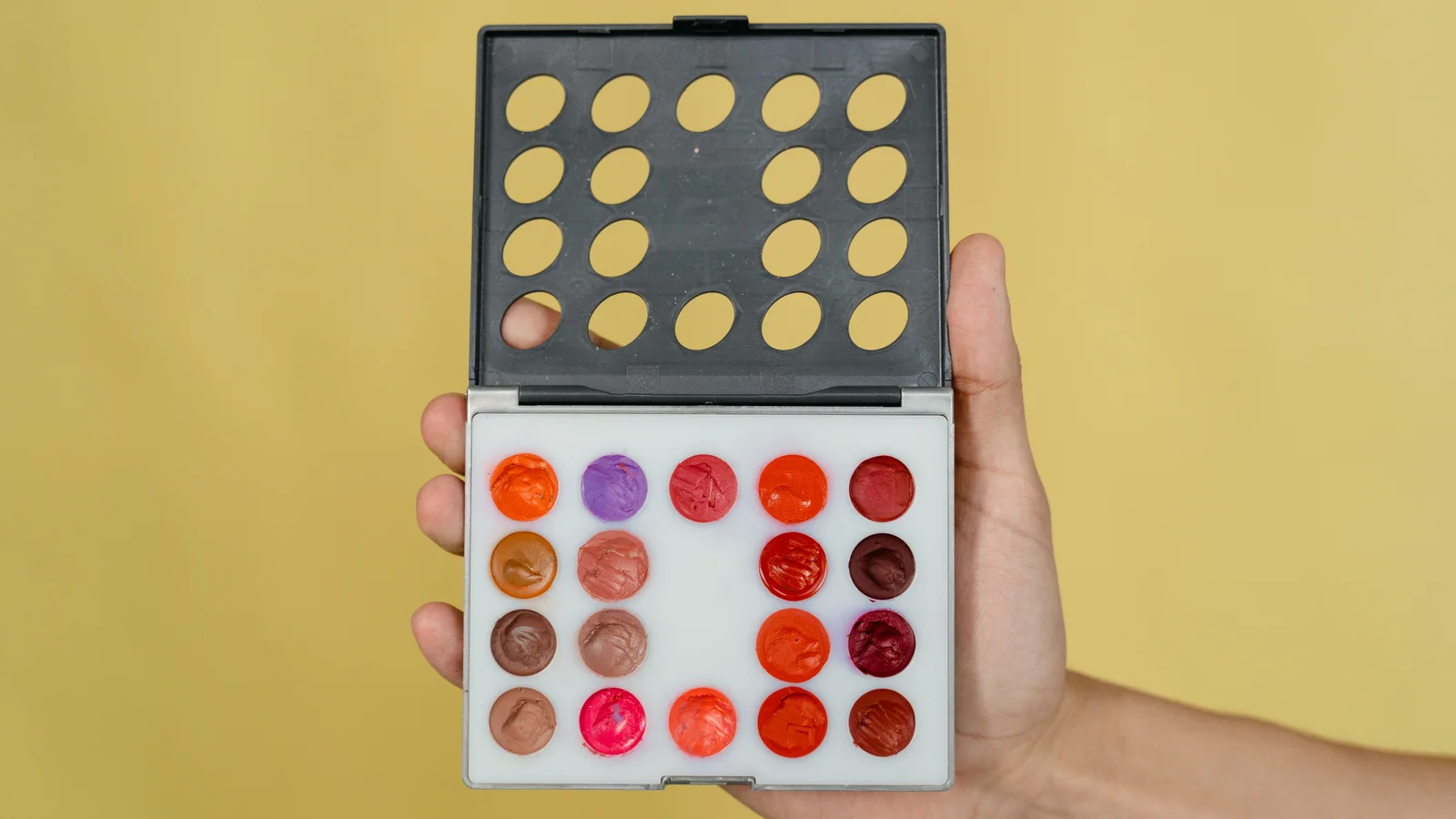 A hand holding an open palette of bright cosmetic colours.