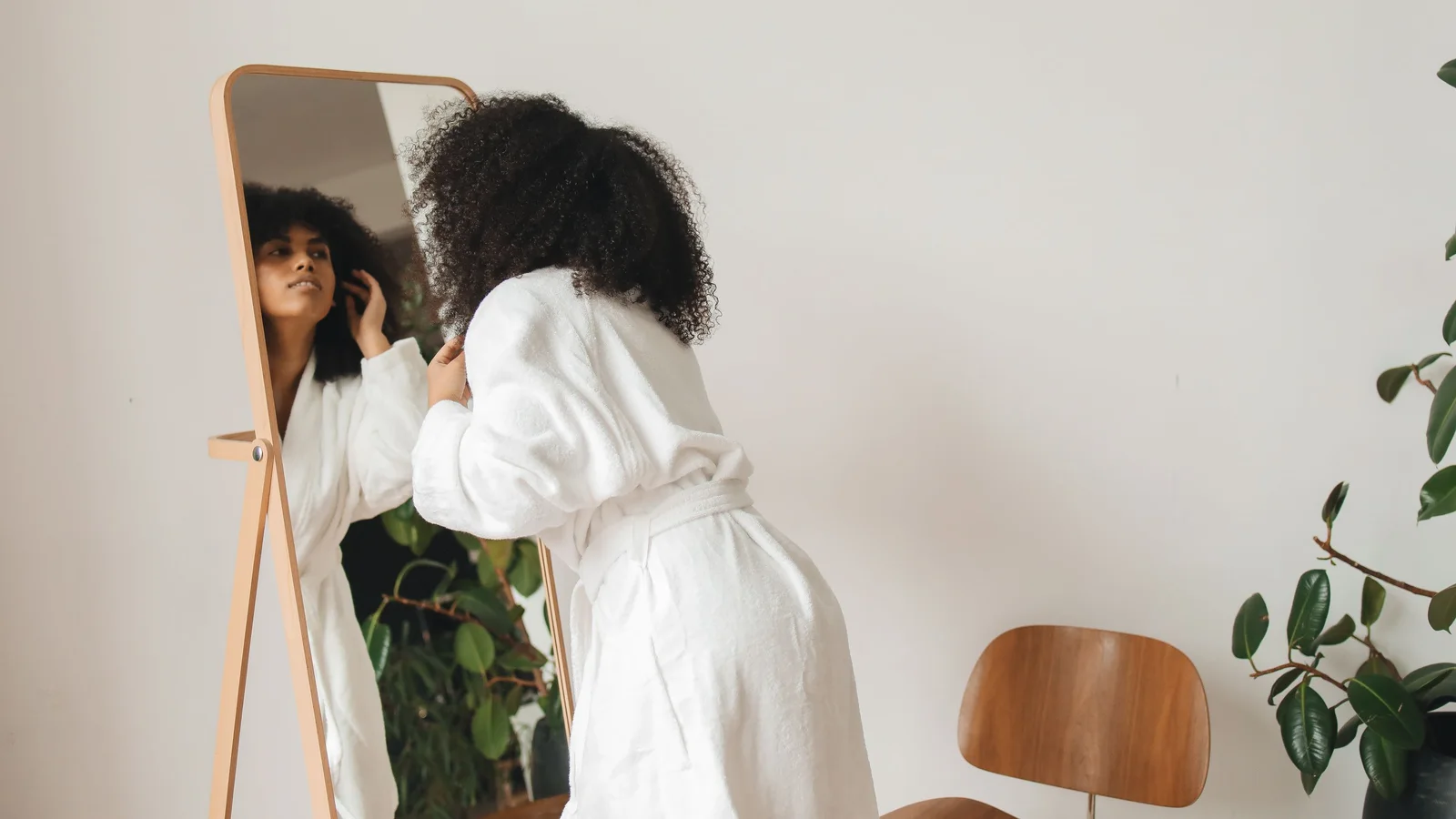 A woman in a white robe leaning towards a mirror during make-up application.