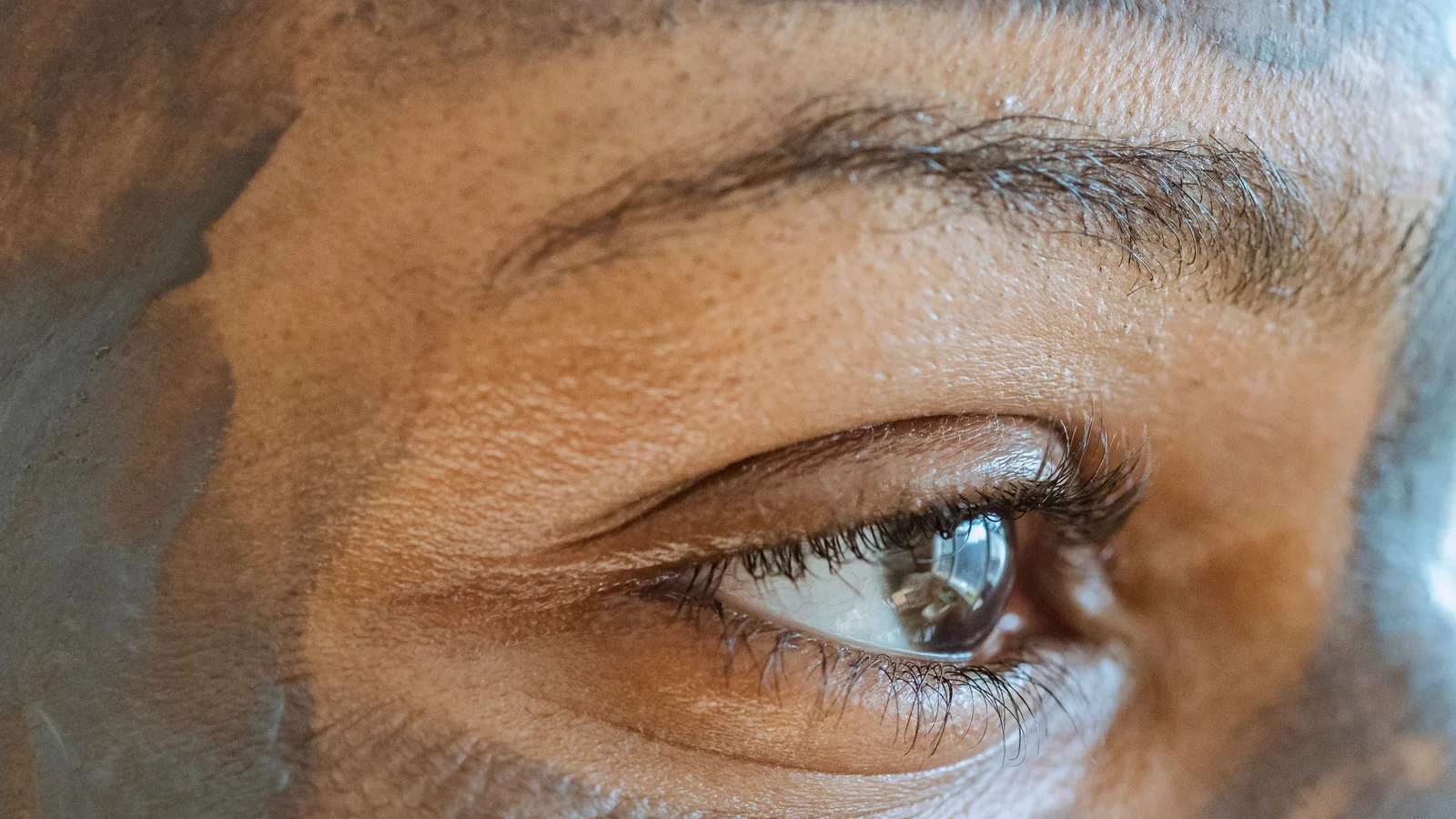 Close-up of a woman's eye and cheek with a grey cosmetic mask visible.