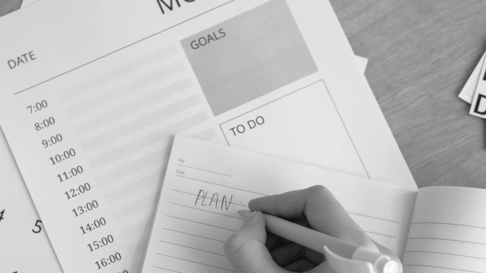 Black-and-white photograph of a hand writing in a weekly planner beside a calendar.