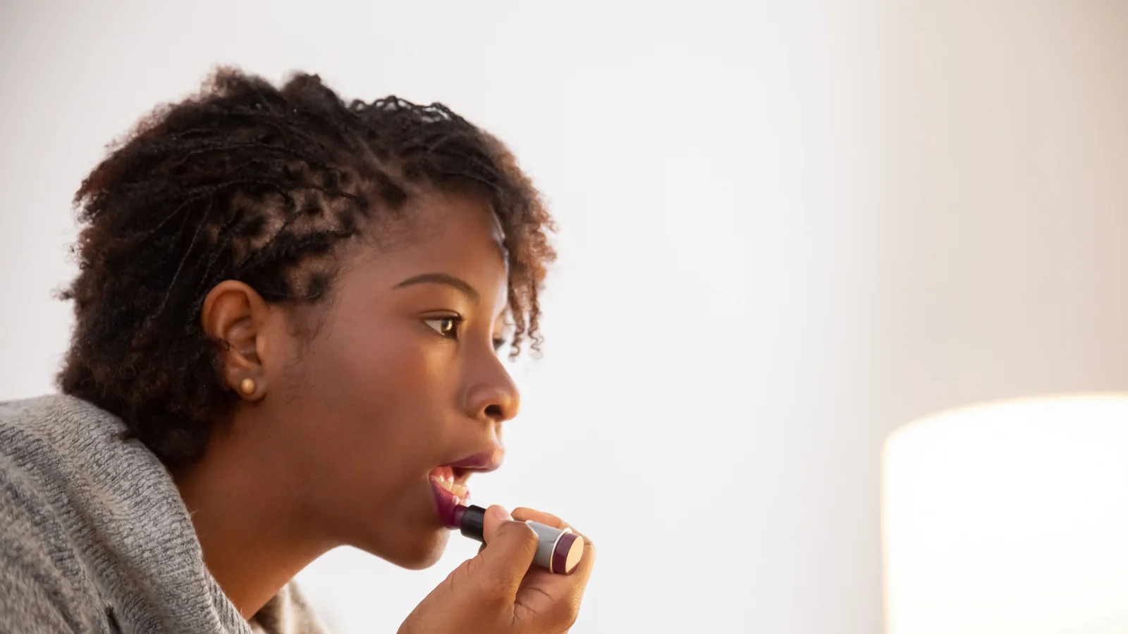 A woman applying lip colour with a small cosmetic applicator.