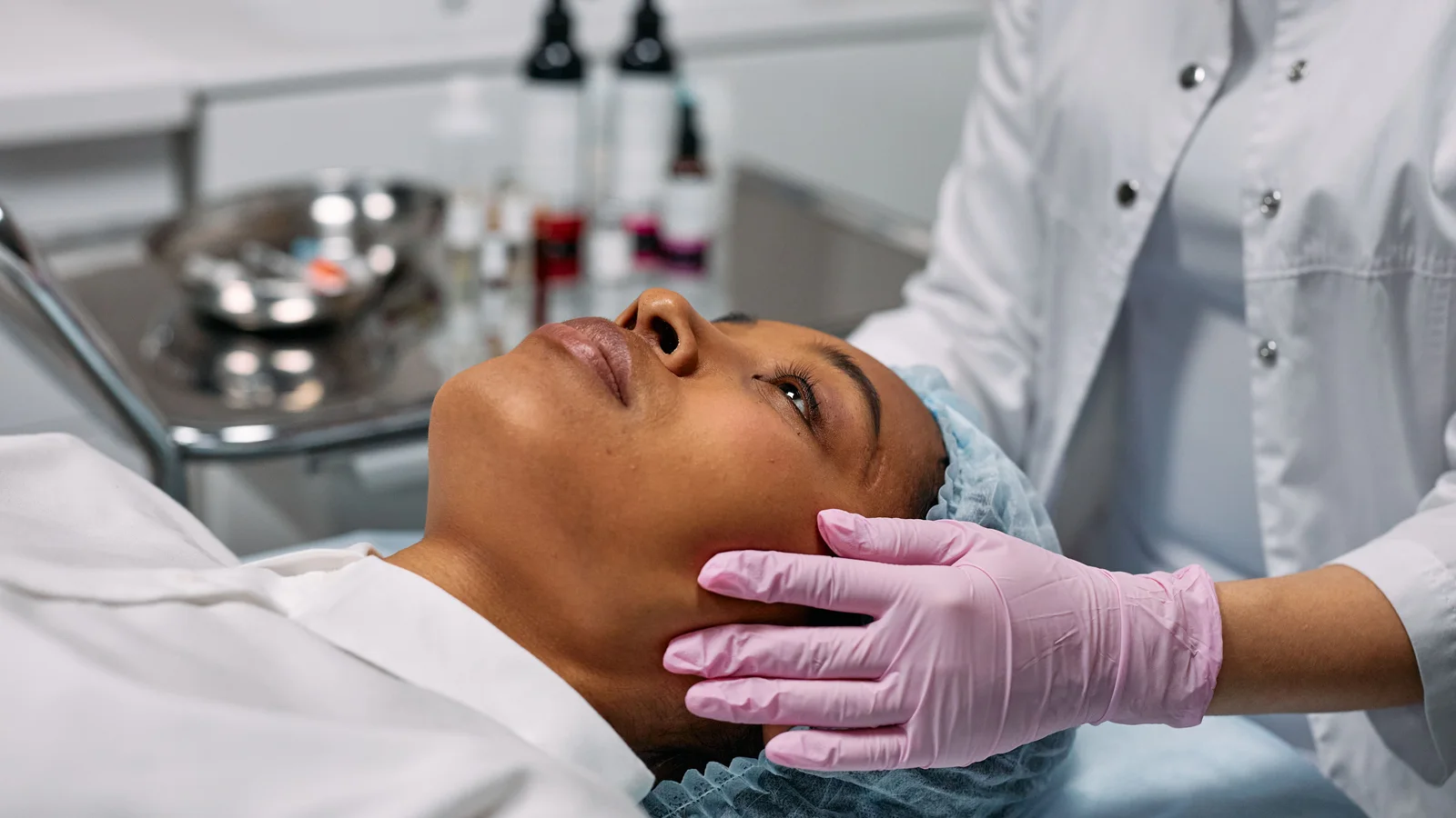 A woman resting on a treatment bed while gloved hands support her face.