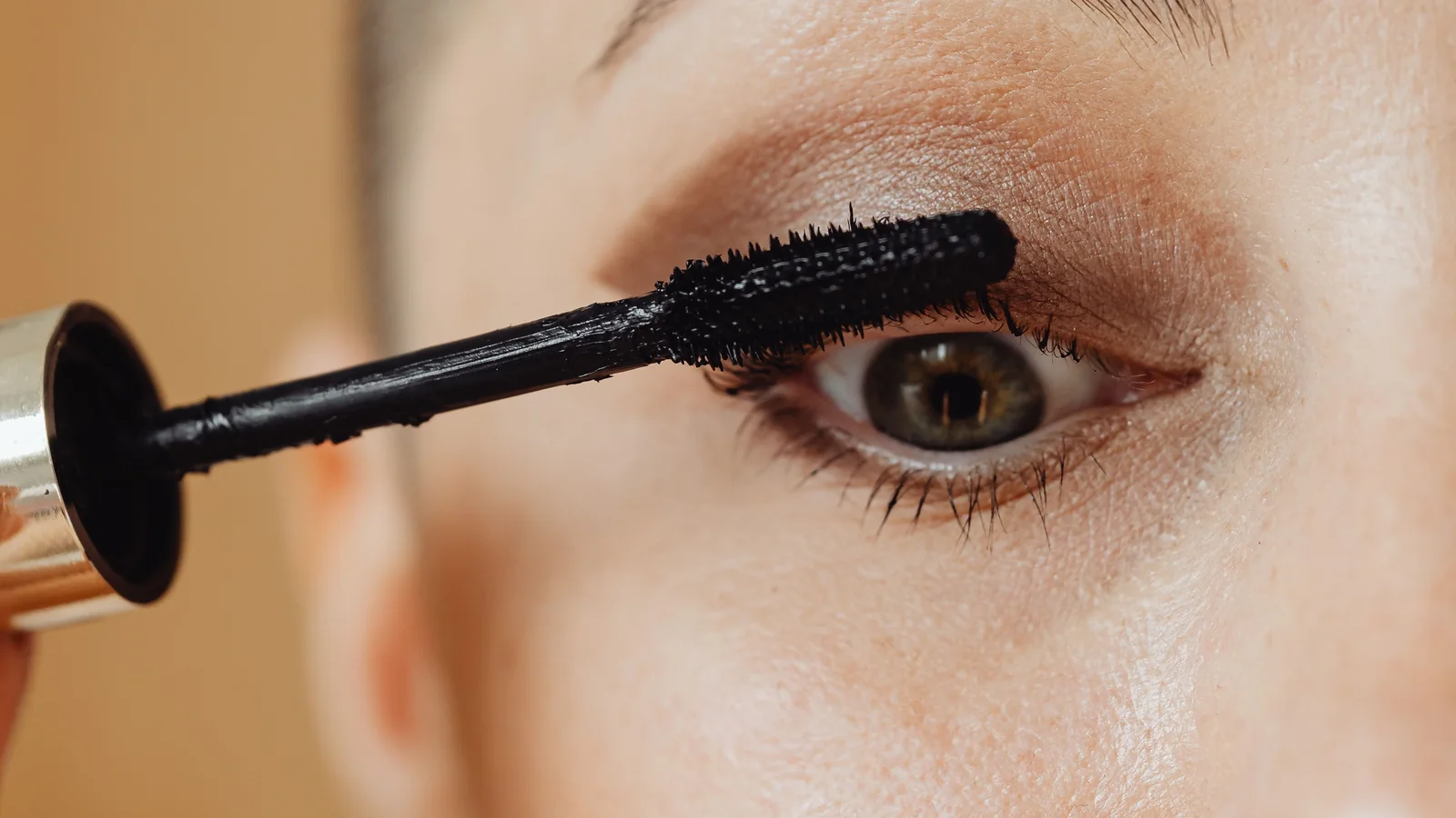 A woman brushing mascara onto her upper eyelashes.
