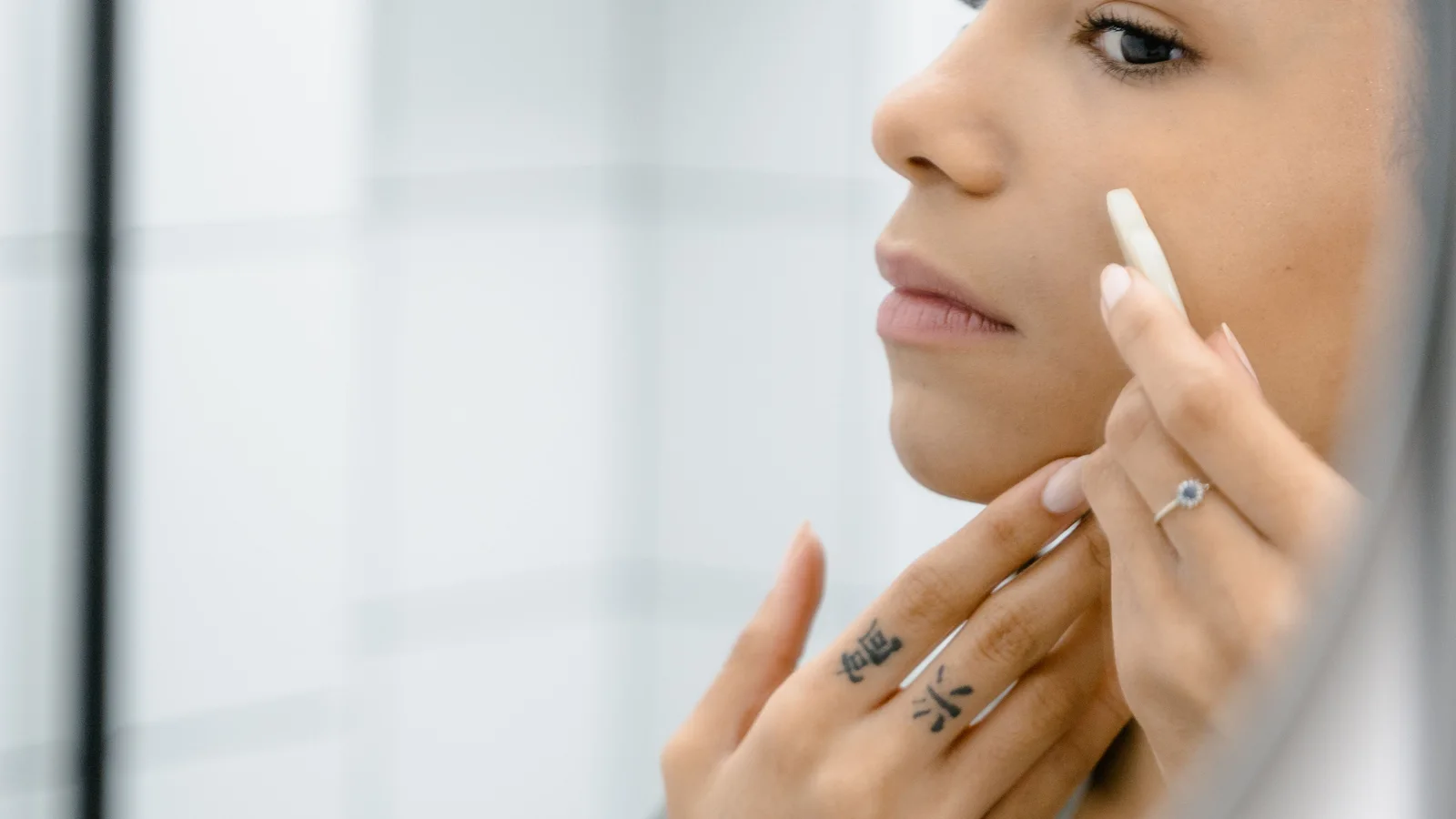 A woman placing a small amount of product beneath her eye while looking in a mirror.