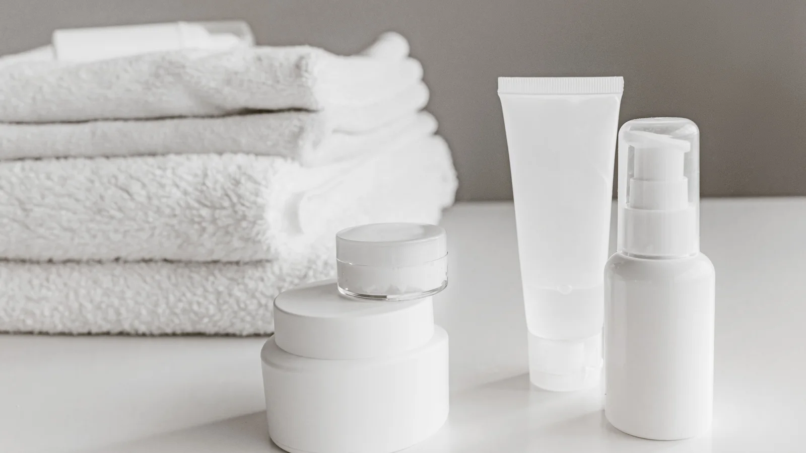 Plain white cosmetic containers beside a stack of folded towels.