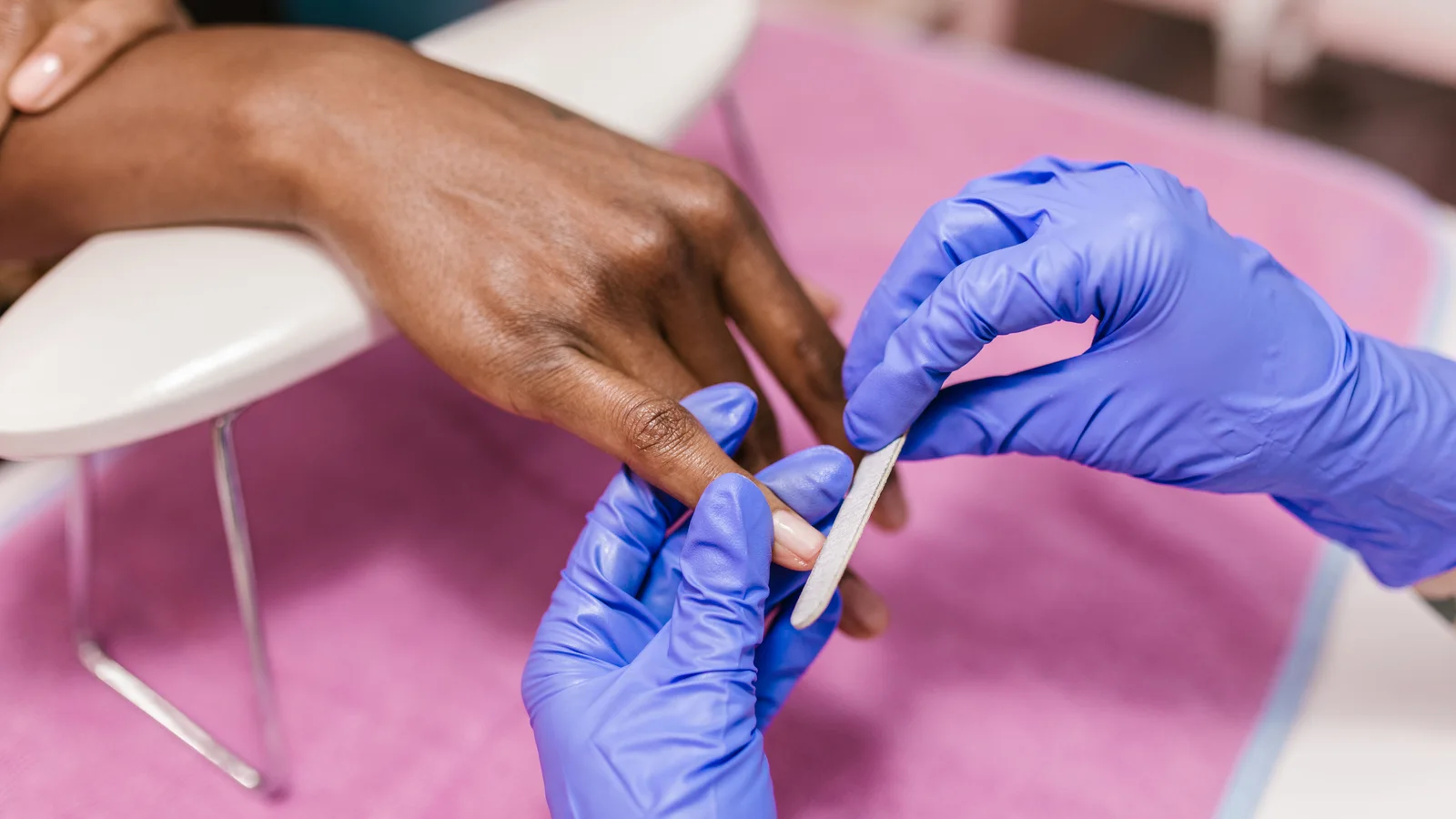 Gloved hands using a nail file during a manicure.