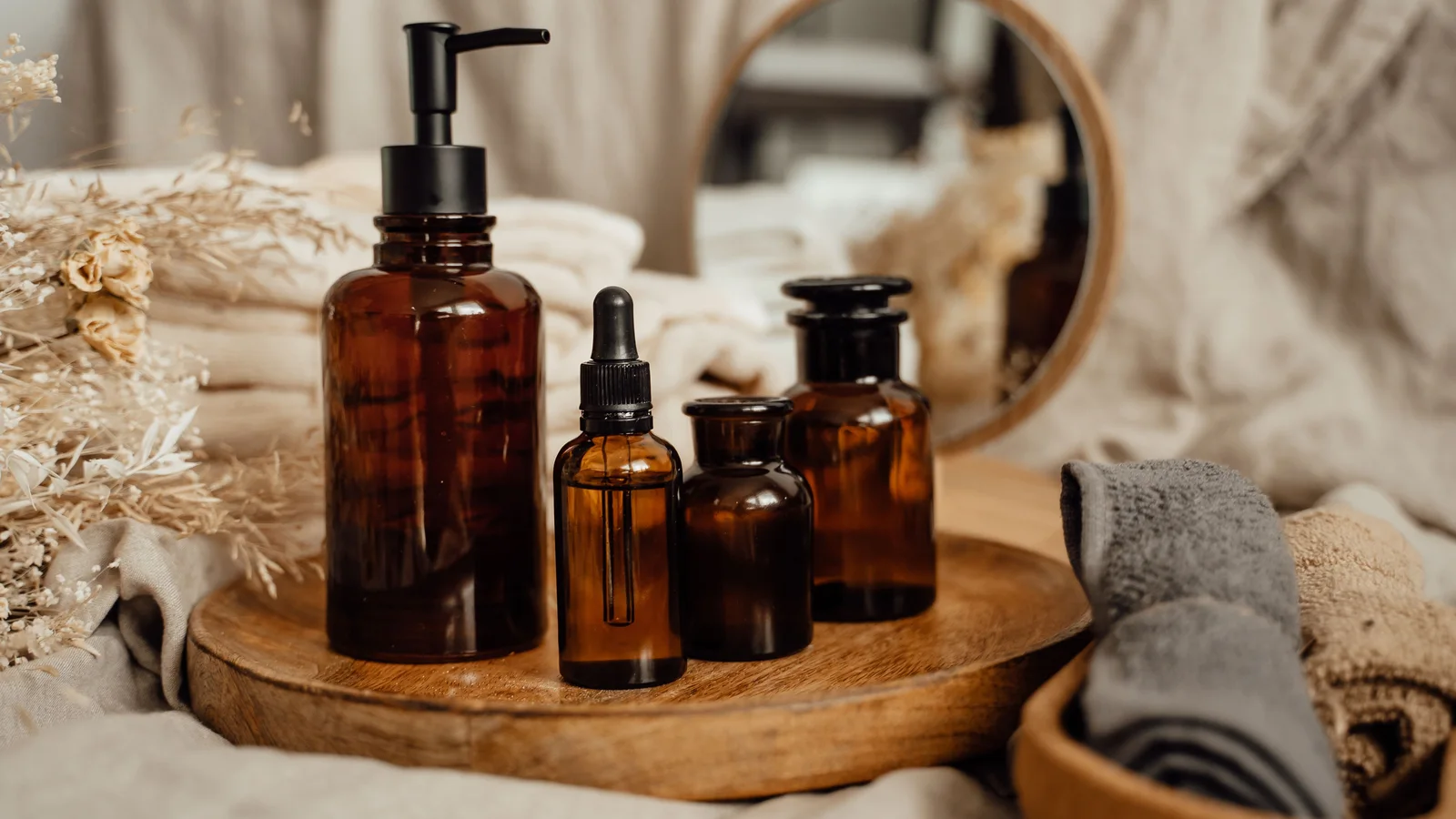 Amber cosmetic bottles beside towels and a round mirror.