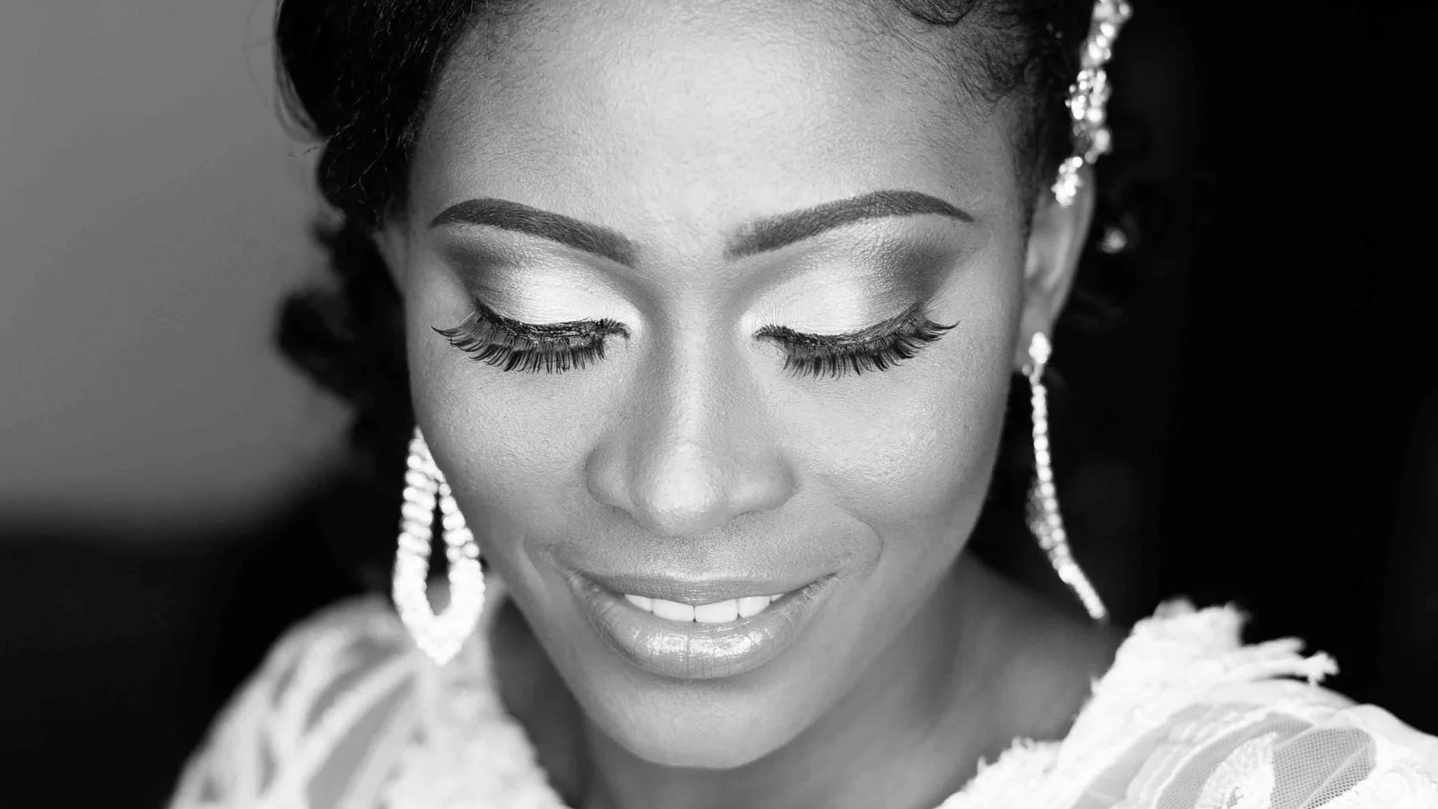 Black-and-white portrait of a woman in a lace bridal outfit with her eyes lowered.