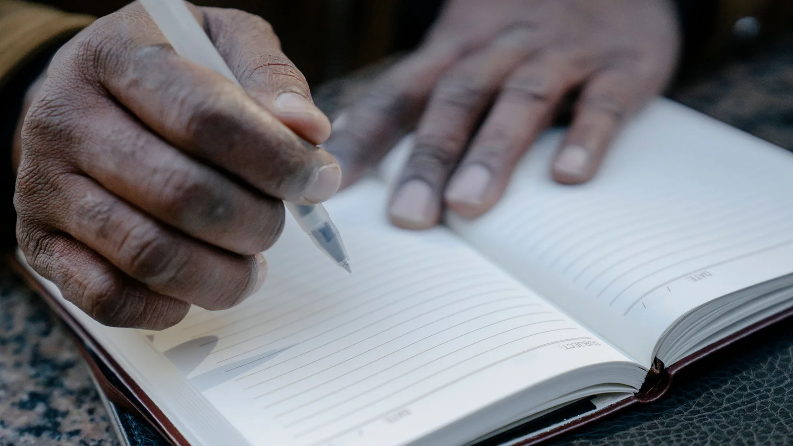 Close-up of hands writing in a lined notebook.