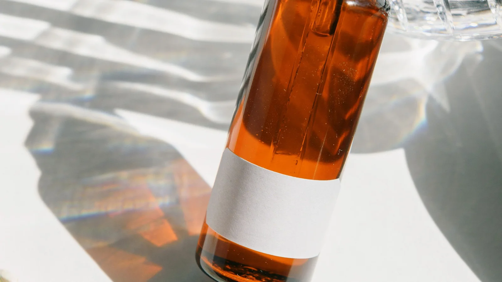An amber dropper bottle with a plain label in patterned sunlight.