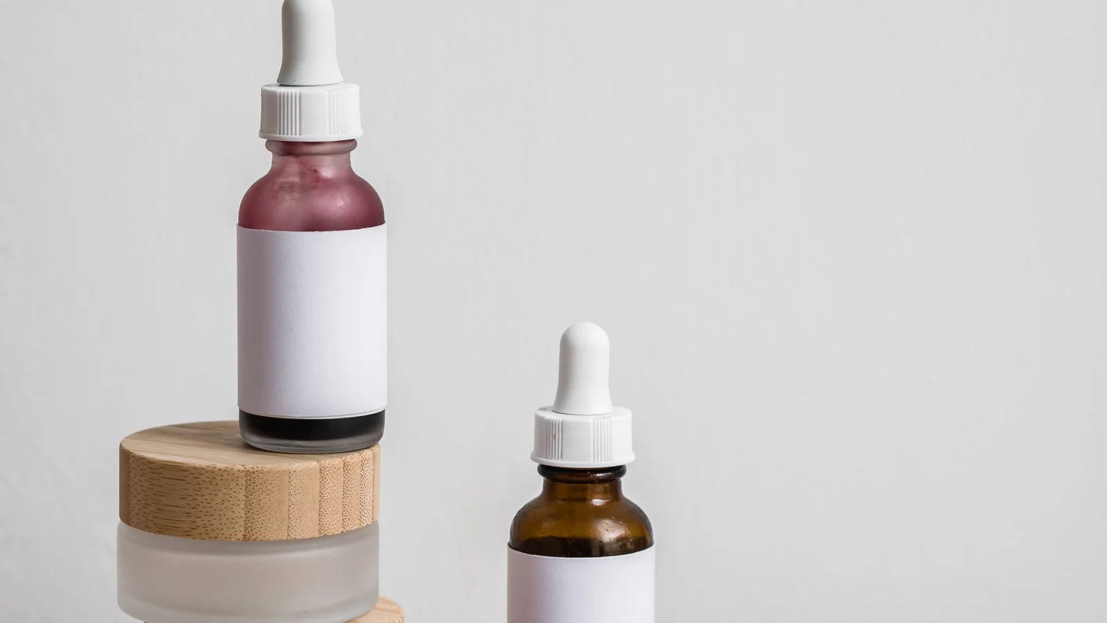 Small cosmetic bottles and a wooden-lidded jar arranged on fabric.