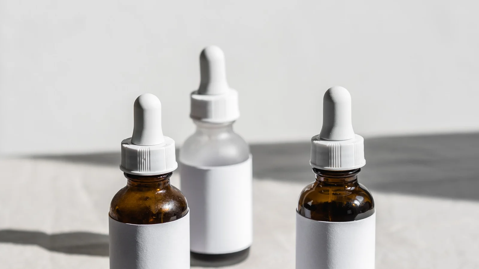 Three small dropper bottles with blank white labels on fabric.