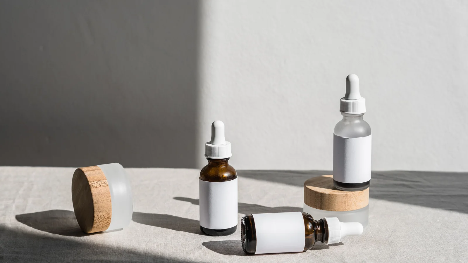 Cosmetic bottles and a wooden-lidded jar arranged in sunlight.