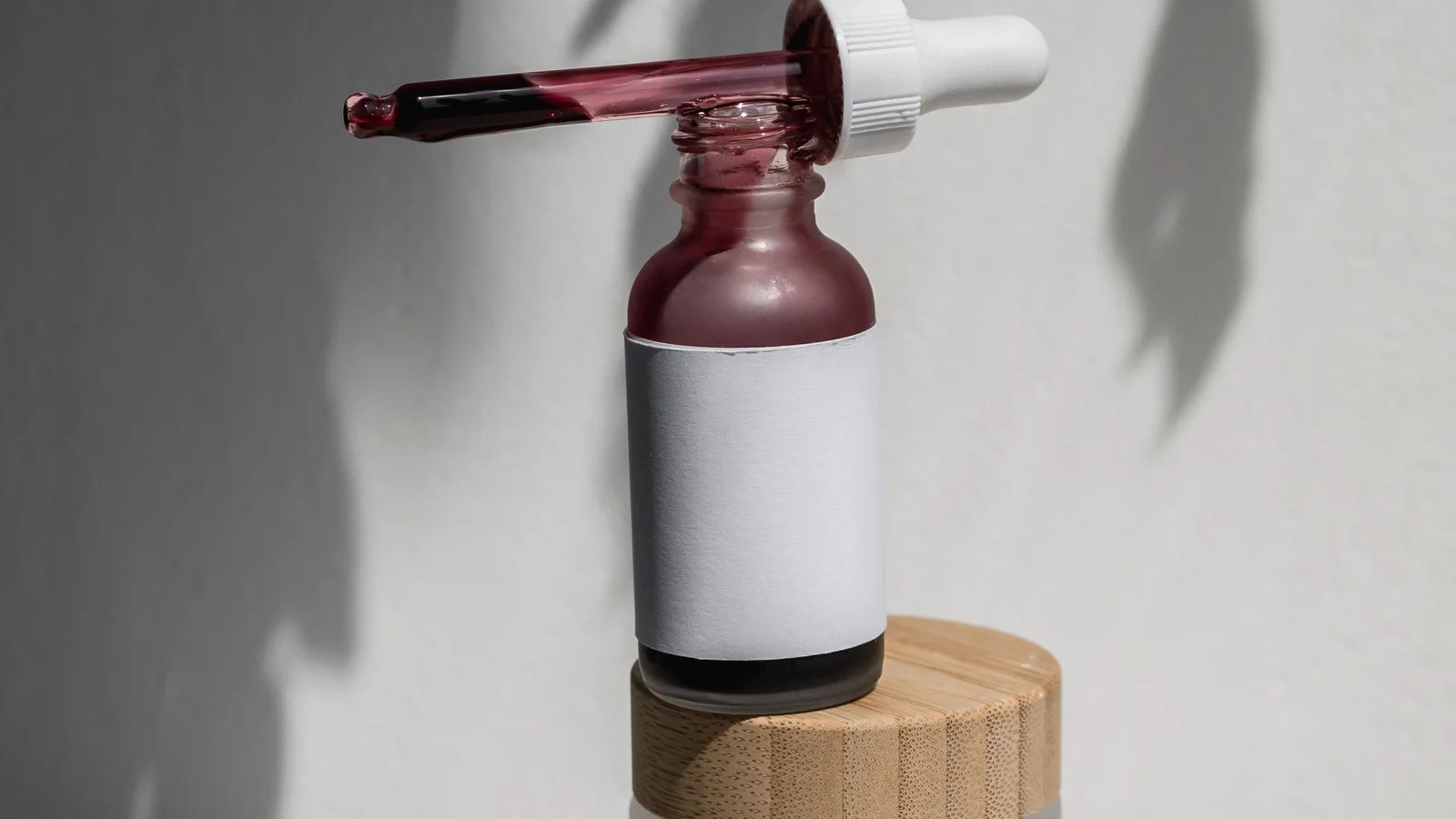 An open dropper beside a cosmetic bottle and wooden-lidded jars.