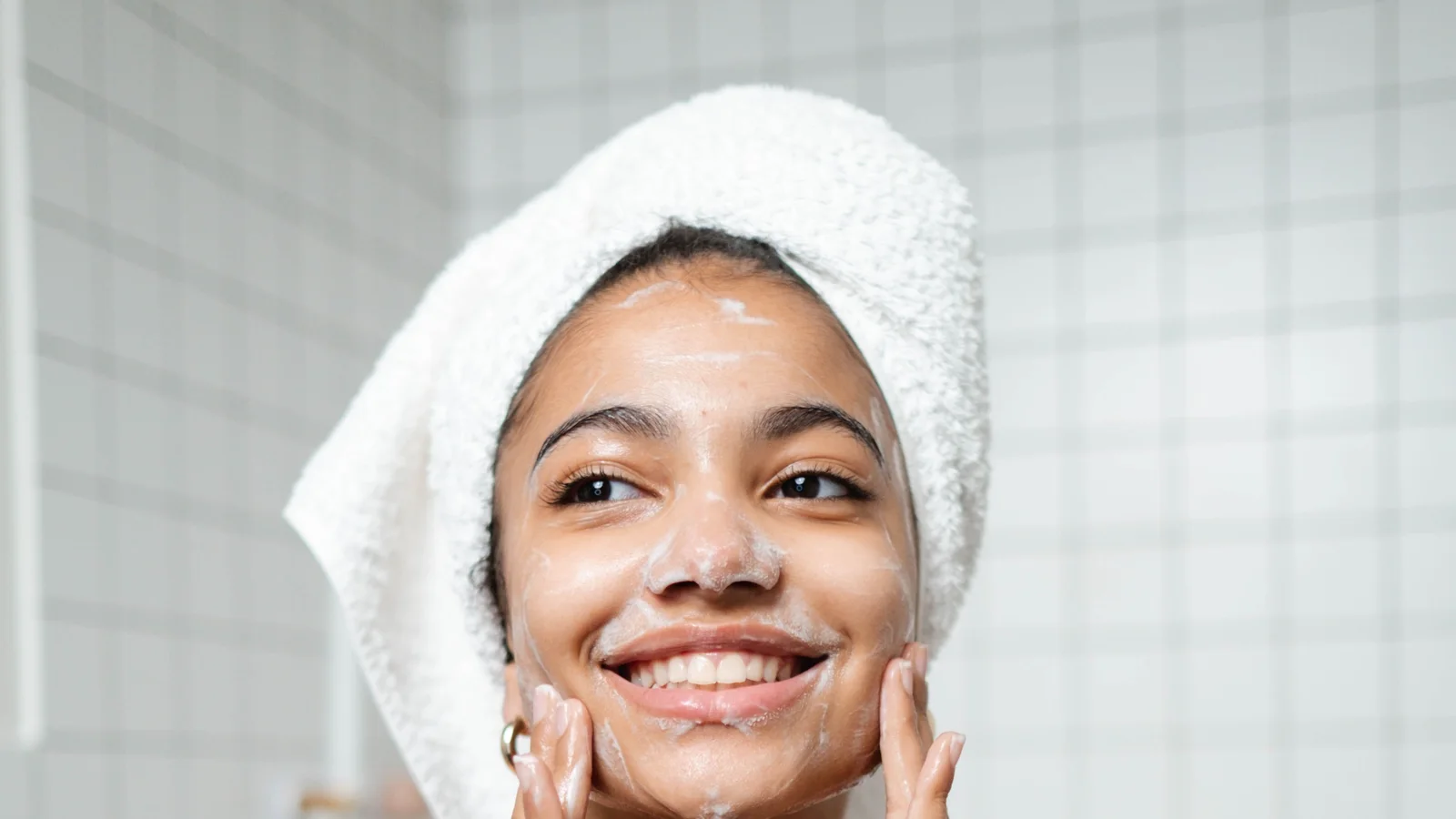 A woman smiling while gently touching both cheeks during skincare.