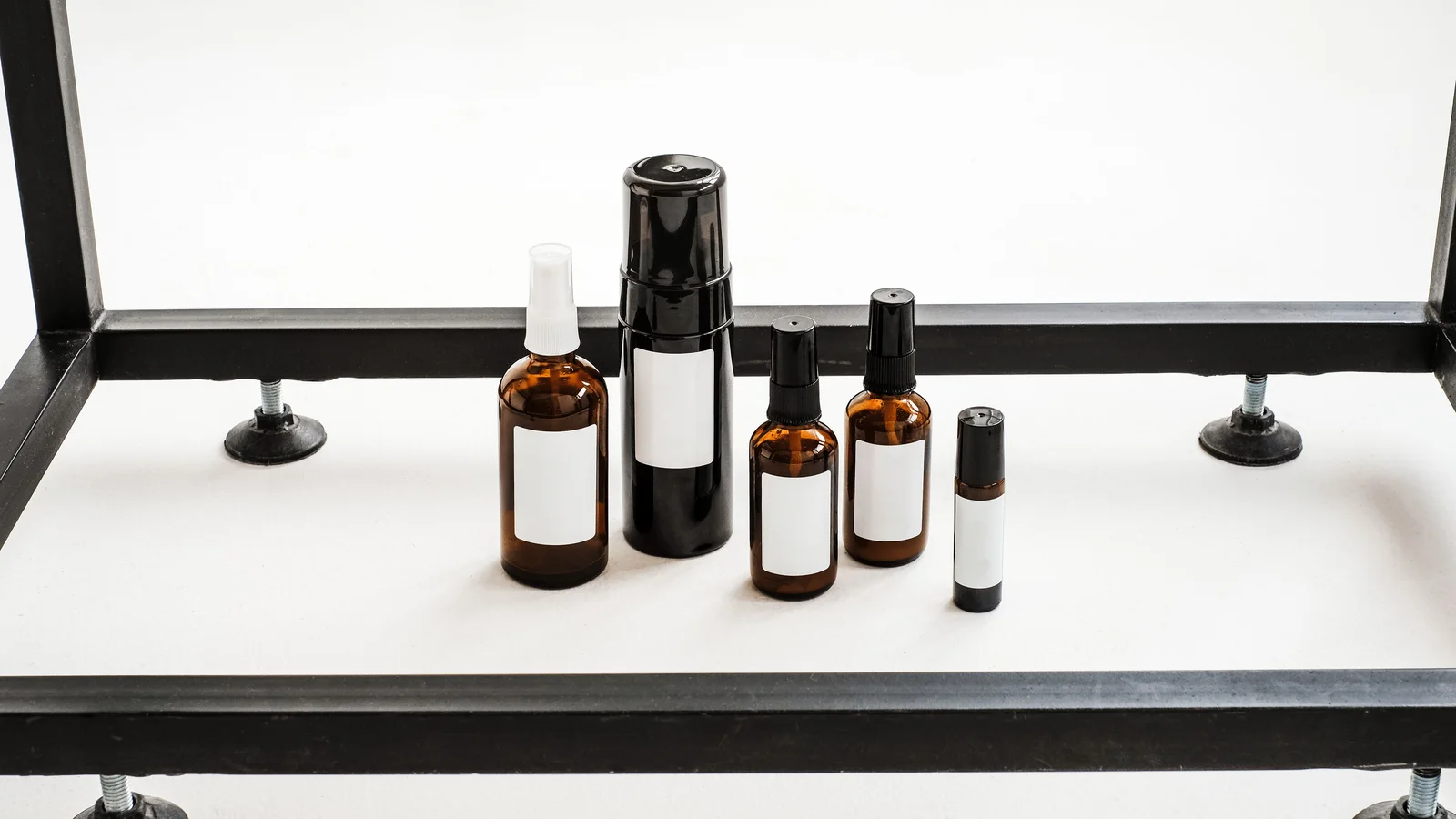 Several amber cosmetic pump and spray bottles on a pale shelf.