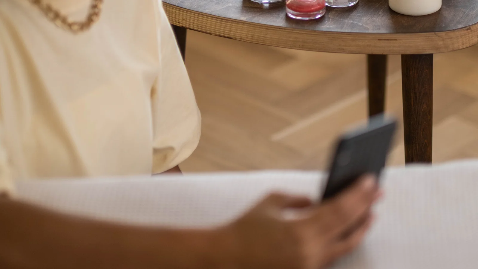 A woman looking at a phone beside beauty products on a small table.
