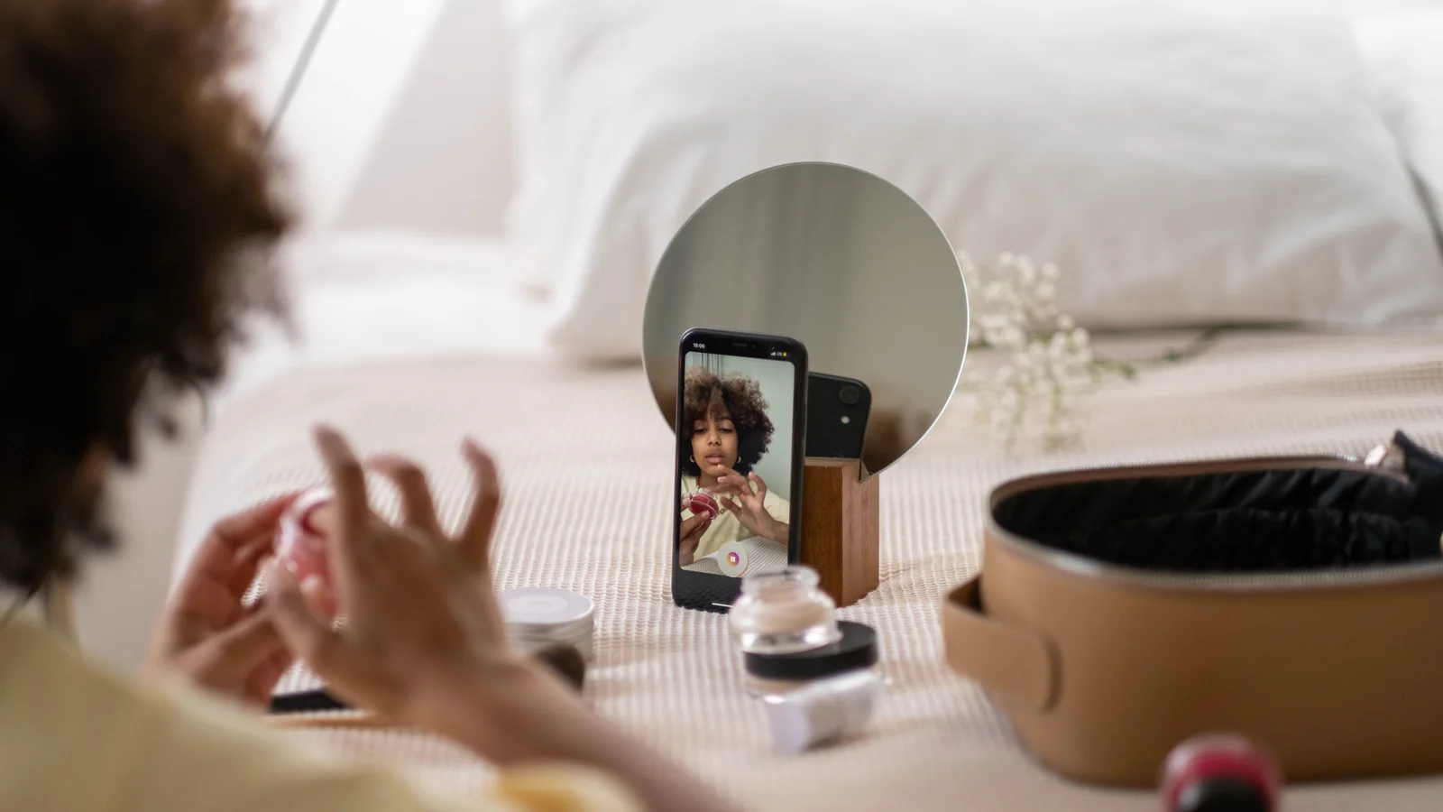 A woman recording a beauty video with a phone on a table.