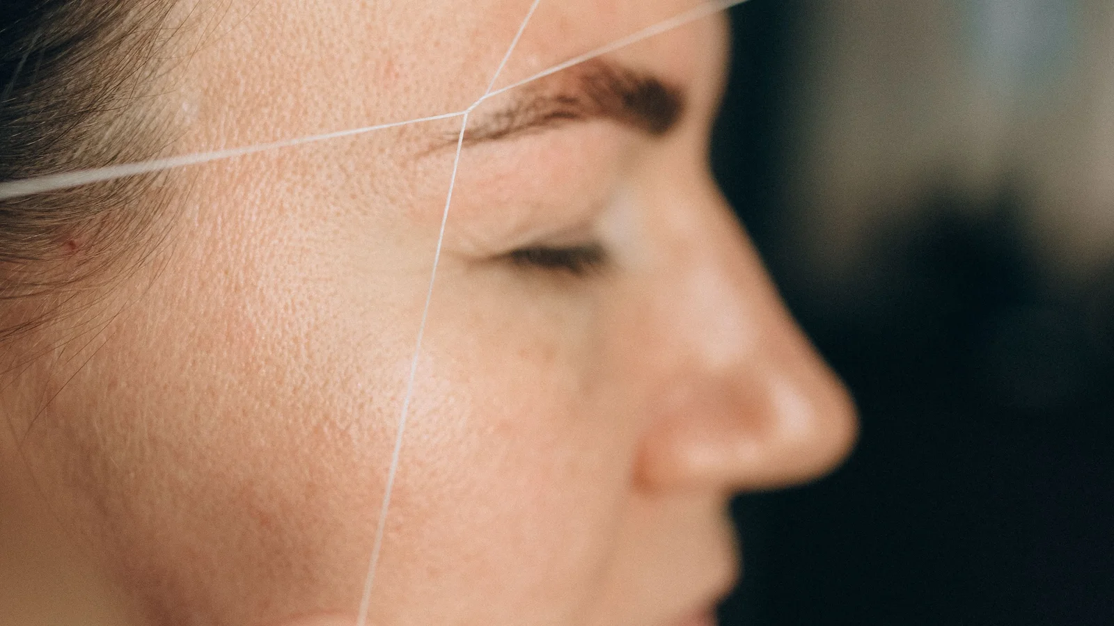A woman having hair around her eyebrow removed with thread.