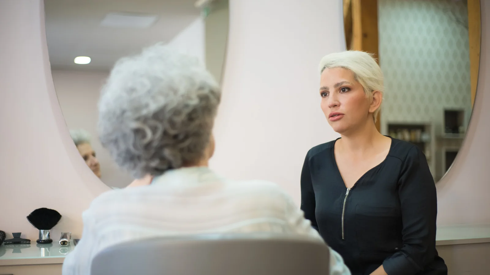 Two women talking while seated opposite each other in a salon.