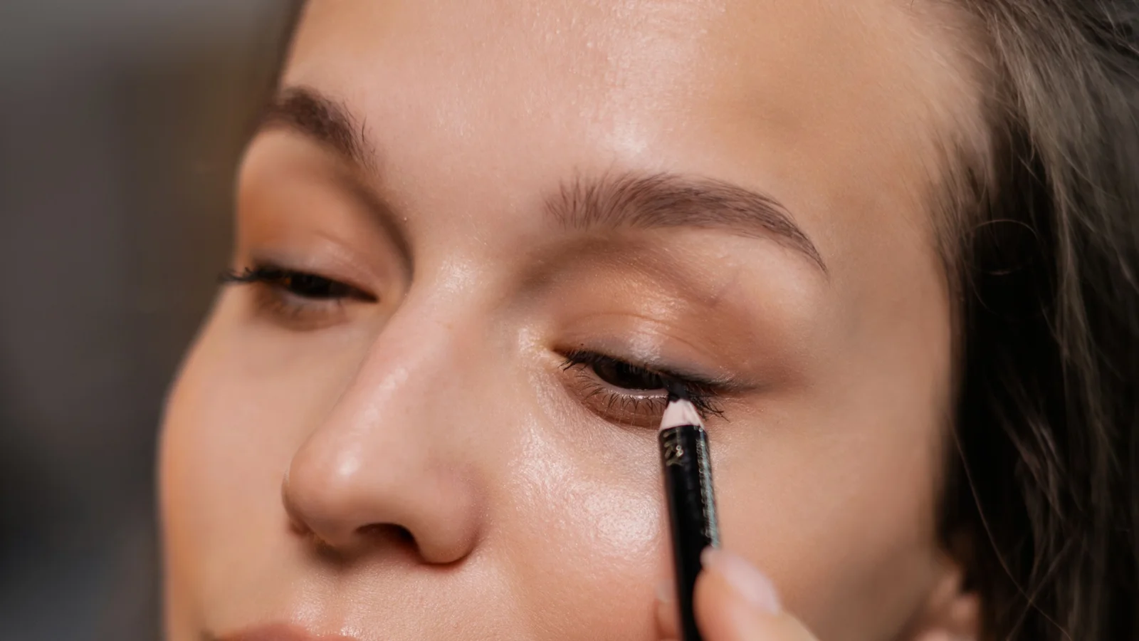 A woman applying dark eyeliner beside her eye.