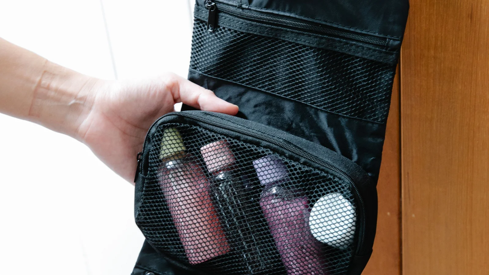 Hands opening a black hanging toiletry organiser on a door handle.