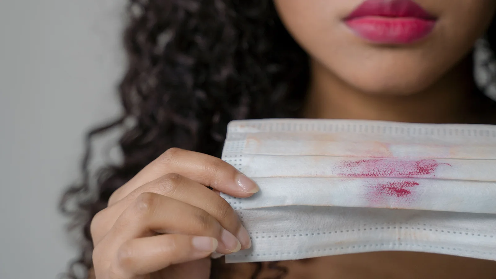 A woman holding a pale face covering with visible lipstick marks.