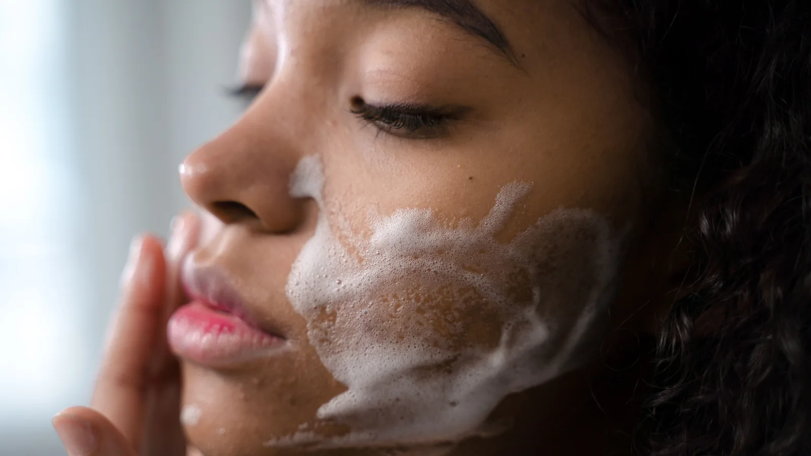 Close-up of a woman applying foaming cleanser to her cheek.