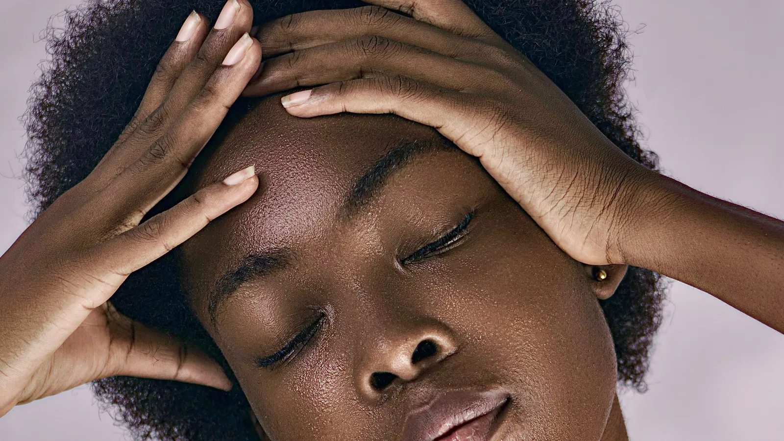 A woman with closed eyes resting her hands across her forehead.