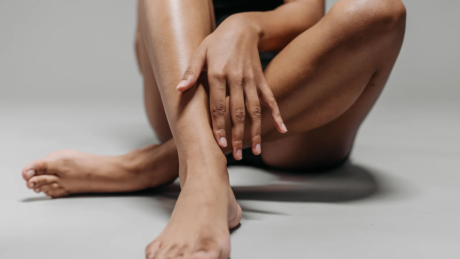 A person seated with crossed lower legs and hands resting on one shin.