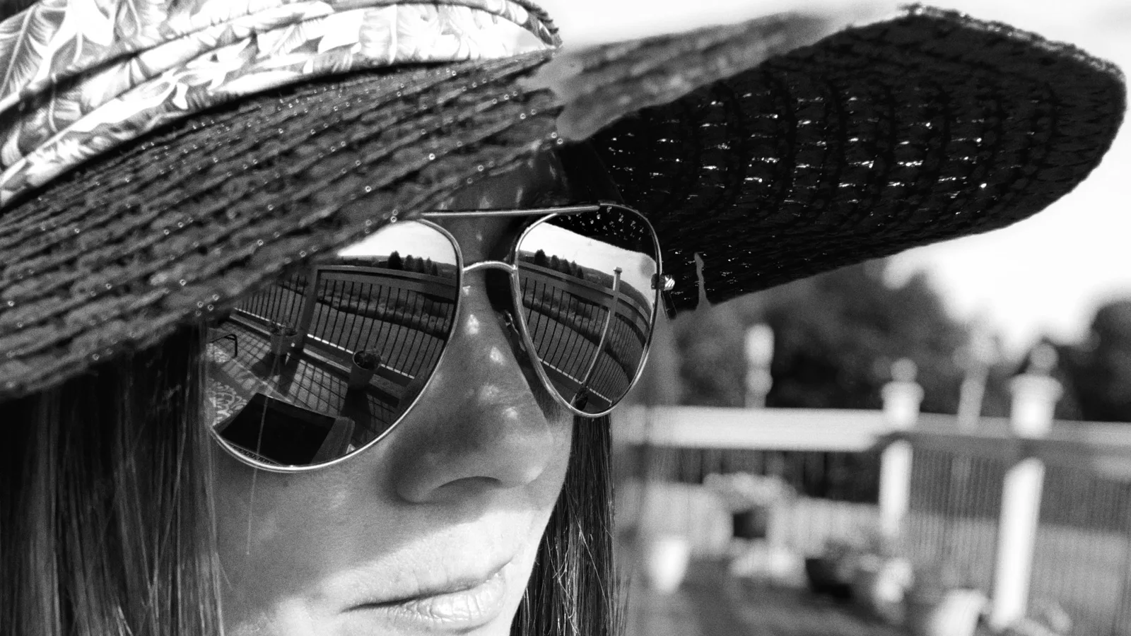 Black-and-white portrait of a woman wearing a broad-brimmed hat and sunglasses outdoors.