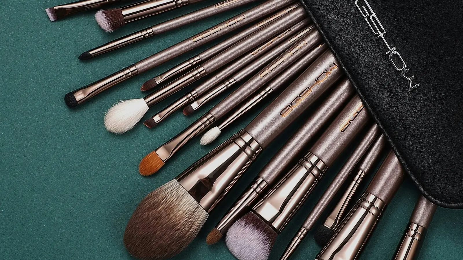 An open black brush case with several make-up brushes on a green surface.