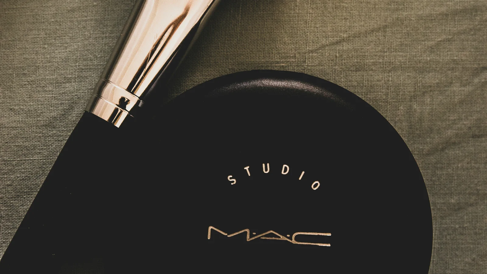 A make-up brush resting beside a black powder compact.