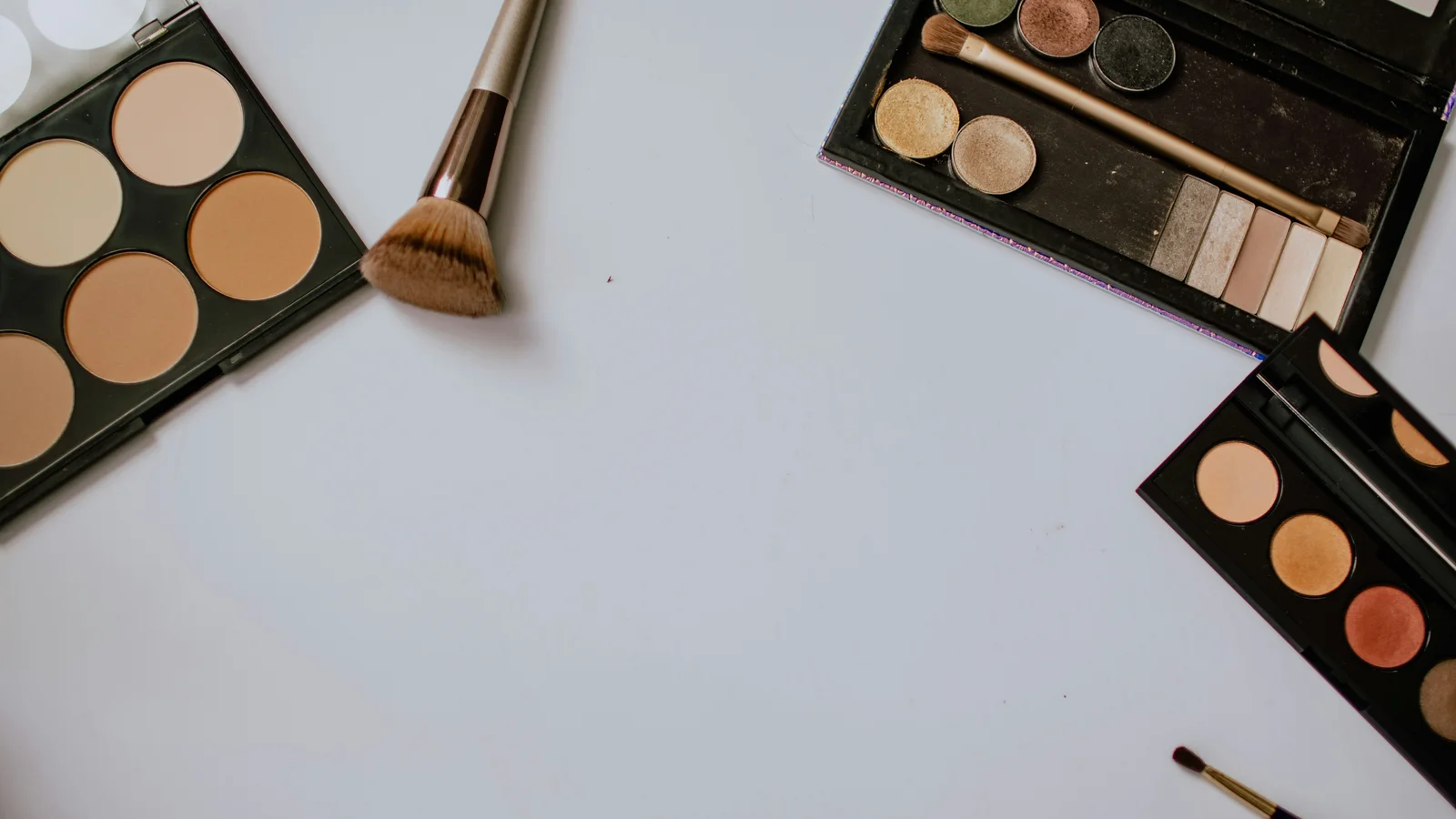 Open colour palettes and make-up brushes on a pale surface.