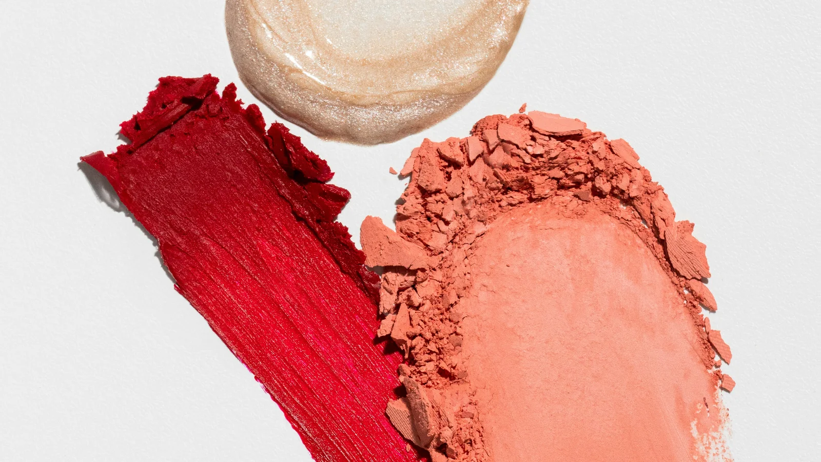 Swatches of red, pink and peach cosmetics beside a pale cream swatch.