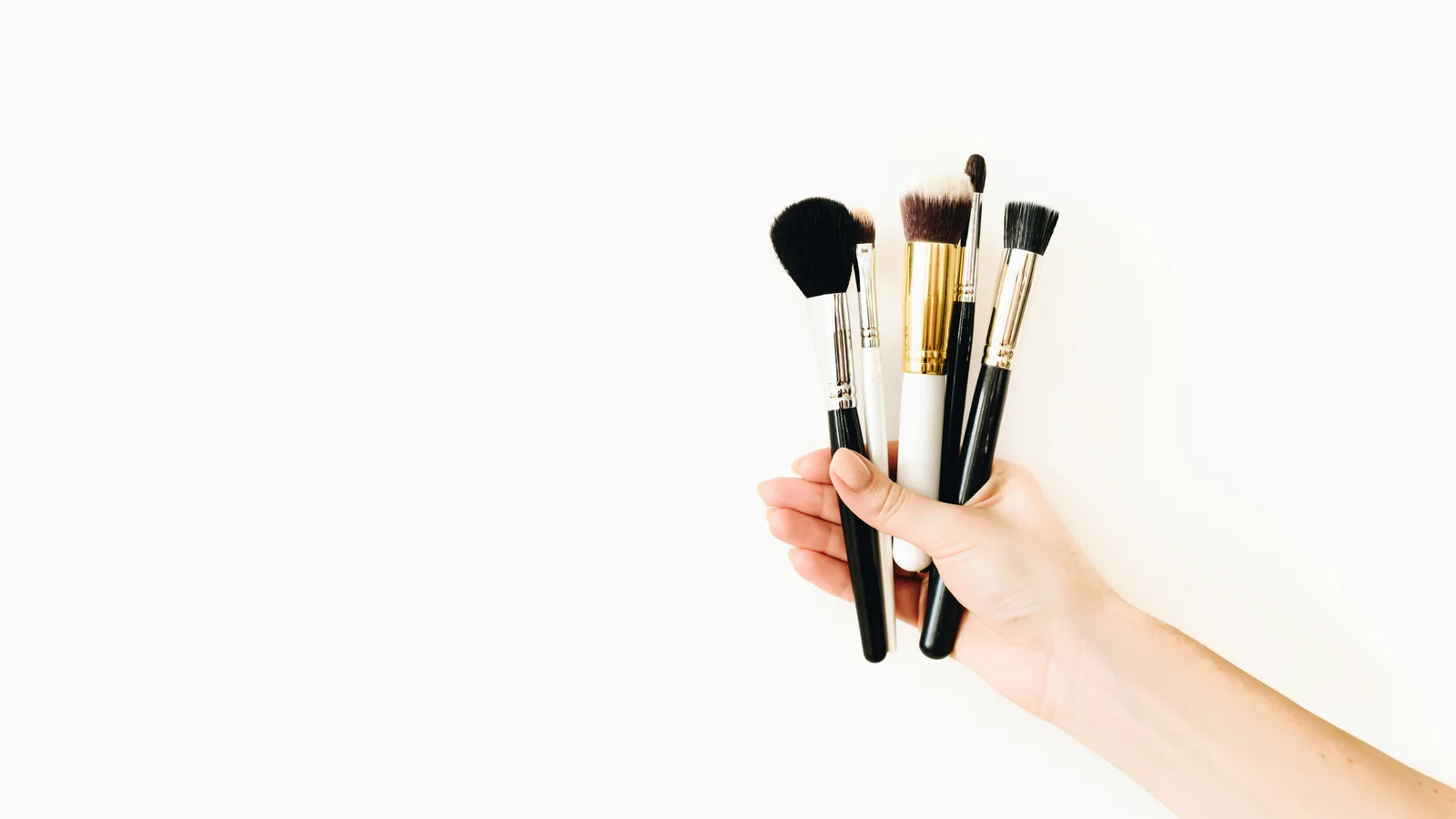 A hand holding several make-up brushes against a white background.