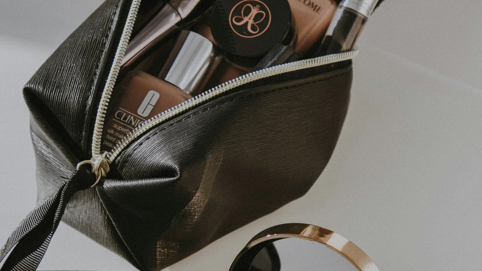 An open dark make-up bag with brushes, cosmetics and a compact nearby.